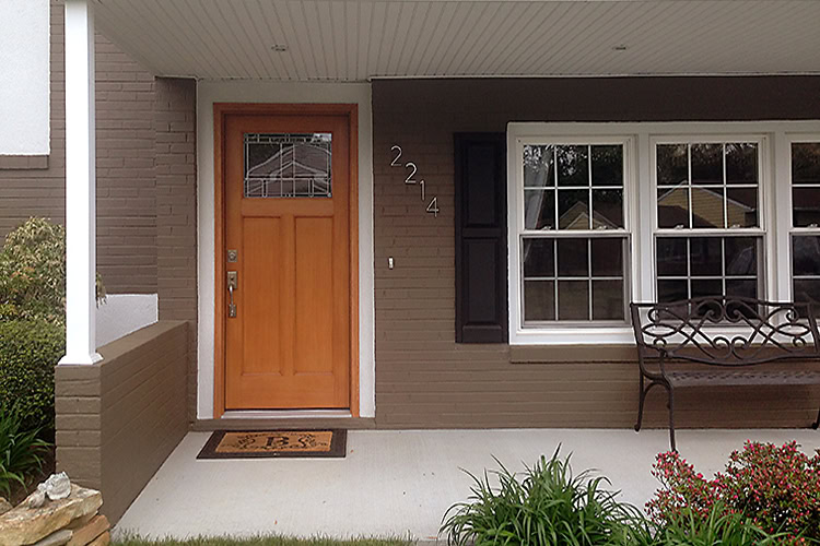 The front porch of a house in DE boasts a brown exterior. A wooden door, doormat, and bench near a window enhance its charm. The house number "2214" is elegantly displayed on the wall, while greenery lines the edge. Residents here have praised the local roof repair services in New Castle County.